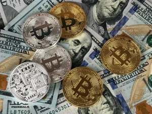 O grămadă de monede aurii Bitcoin așezate peste bancnote de dolari americani, simbolizând tranziția dintre sistemul financiar tradițional și economia digitală, cripto.