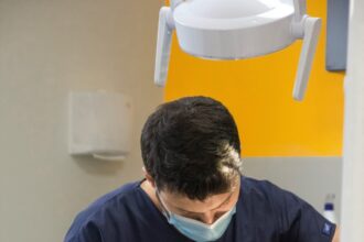 Pacient pe scaun stomatologic, medic dentist în halat și mănuși efectuând o procedură cu echipamente moderne.